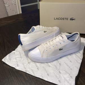 Lacoste skor i mycket bra skick! Tygsko med gummi på tån och blå stripe på hälen samt blå sula och blå ”Lacoste” text, skorna är sparsamt använda och säljs med original box, perfekta skor nu till sommaren!  Köptes för 1300 jag säljer dom för 549. 
