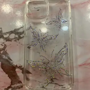 Den är genomskinlig och är för iPhone 14. Med fjärilar av pärlor på.