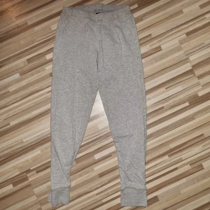 Grå mjukisbyxor - Ett par bekväma grå tunna mjukisbyxor med elastisk midja och muddar vid bensluten. Byxorna har en avslappnad passform och är perfekta för vardagsbruk eller träning.