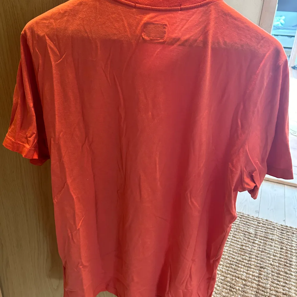 mycket bra skick, knappt använd. En orange t-shirt från C.P. Company med ett tryck av en figur och texten 'C.P. Company' på framsidan. T-shirten har korta ärmar och en rund halsringning. . T-shirts.