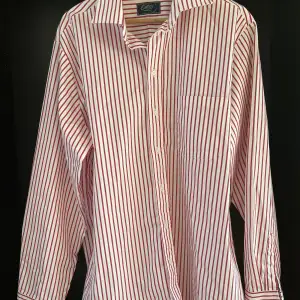 En jättefin skjorta från Oscar i klassiskt vit med röda ränder. Använd endast en gång då den tyvärr inte passade mig. Dyr i inköp.  Storlek 43(CL) med fin passform. 