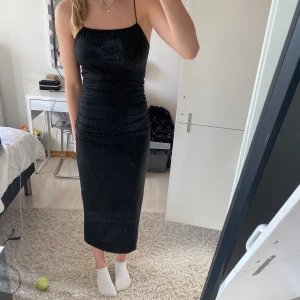 Svart klänning - Svart klänning med öppen rygg och en ”knut” i svanken, tunna gummiband längs axlarna och en slits vid höger ben! Använd endast ett fåtal gånger och superskönt material🩶 (Nypris 159kr)