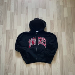 Weekday Graphic Zip Hoodie - 399 - Svart Weekday zip hoodie t i storlek Small. 80% bomull, 20% polyester blend. Rött/vitt broderat tryck över bröstet. SAB dragkedja & snören för att anpassa luvan 