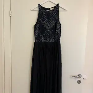 Festlig mörkblå långklänning med vackra detaljer från Lace & Beads, storlek M. Klänningen är som ny, använd enbart 2 ggr.  Dragkedja bak. Paljetter fram och bak.   Mått: längd ca 150 cm, midja ca 37 cm, byst ca 45 cm