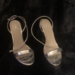Klackskor  - Silvriga klackskor med öppen fot. Dem är i storlek 38 och har tunna band som går runt foten. Skulle gissa på att klacken är runt 10 cm