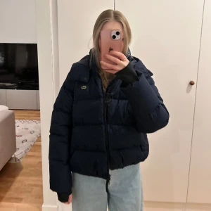 jacka från Lacoste - Mörkblå pufferjacka från Lacoste med hål för tummarna. Använd men i bra skick. Storlek XS, passar XS-S. Älskar den här jackan!