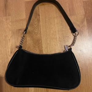 Svart handväska - Svart handväska i mocka textur, med små kedje detaljer på remmen