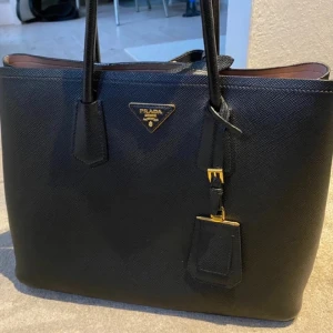 Pradaväska - Väldigt fin Saffiano väska (Large). Några märken invändigt. Köpt 2016 i London för 1,865 dollar vilket motsvarar idag cirka 24712kr.  Kvitto finns dock något solblekt. Avtagbar axelrem.