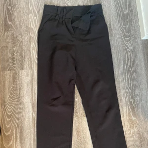 Kostymbyxa från Bikbok  - Kostymbyxa från Bikbok. Storlek XS men passar en 36/38. Svart/bruna. Har tidigare vara ett rosettskärp men det har tappats bort. Men de kan användas ändå. Säljer för 50kr. 