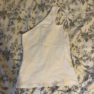 Oneshoulder topp - Säljer detta jätte finna oneshoulder linnet, med två ”remmar” på ena axeln. Kan stylas med jeans, kjolar, shorts eller bara ett par byxor. Använd 2-3 gånger. Ej genomskinlig!