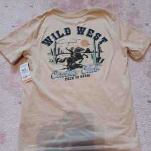 Helt ny cool cowboy cowgirl tshirt från USA - Säljer denna helt nya supercoola och unika t-shirten med rodeo / cowboy motiv, ett litet trtck fram och ett större på ryggen. Den är från Target i USA, helt ny och lappen finns kvar! Storlek 160 vilket är ungefär samma som xxs eller en tajt xs.