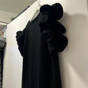 Klänning - Svart stickad klänning med volanger på ärmarna. Strl M