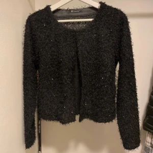 Fluffig kofta  - En superfin kofta från Elinette som är svart med små skymtningar av klitter, tyvärr finns ingen lapp med storlek på men tror att den skulle passa en XS - S  Bredd- 42 cm. Längd- 47 cm