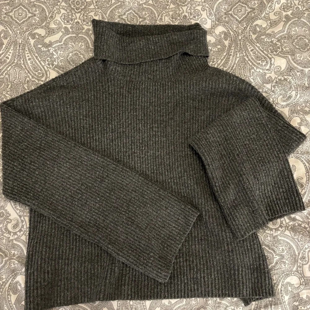 En grå stickad tröja med krage som är lite kortare i längden med bredare ärmar . Stickat.