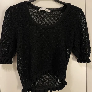 Svart spets topp från Zara - Säljer en snygg svart spets topp från Zara. Den har korta ärmar och en rund halsringning. Den är dekorerad med volanger vid ärmslut och nederkant. Perfekt en utekväll!
