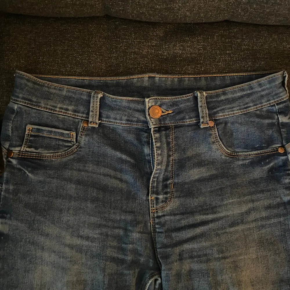 Ett par blå jeansbyxor med hög midja och skinny passform. Byxorna har en dragkedja och knapp framtill. De är i välanvänt skick med synliga tecken på slitage vid fållen.. Jeans & Byxor.