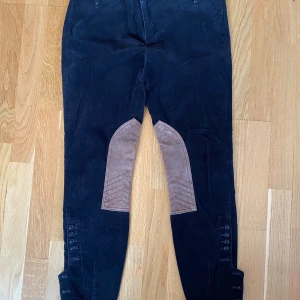 Svarta manchesterbyxor från Ralph Lauren - Svarta manchesterbyxor i ridbyxor modell fr Ralph Lauren i strl 6. Använda men i fint begagnat skick.  Mått  Midjan: ca 43 cm Längd från grenen och ner: ca 72 cm  98% bomull och 2% elastan samt skinn vid knäna 