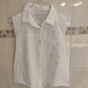 Armlös blus - Vit armlös blus med knappar, och en liten ficka i fram. Hyfsat ny.