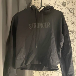 Svart hoodie från Stronger - Säljer en svart hoodie från Stronger. Den är croppad och har en luva med dragsko. Perfekt för en avslappnad och bekväm stil. Passar bra till både vardag och träning.