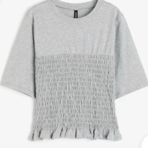 Hm grå smockad tshirt - Säljer den slutsålda trendiga tshirten från Hm. Använd ca 2ggr så i mycket bra skick. Jättesnyggt till hösten, styla med ett par Jeans!