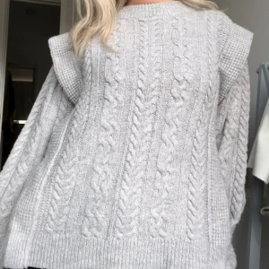 Grå stickad tröja - Säljer en supermysig grå stickad tröja. Den har ett snyggt flätmönster på framsidan och är perfekt för kalla dagar. Tröjan är långärmad och har en normal passform. Perfekt för höst och vinter! 🧶
