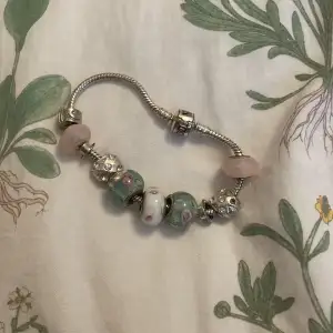 Säljer ett superfint Pandora armband med olika pärlor och blommor. Armbandet är i silver och har flera charmiga pärlor i rosa och grönt med blommönster. Perfekt för att ge en personlig touch till din stil! den sitter löst och kan öppnas ! 