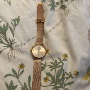 Elegant guldarmbandsur - Säljer en elegant klocka med guldarmband och vit urtavla. Klockan har en stilren design med ett mesharmband i guld och en enkel urtavla med guldmarkeringar. Perfekt accessoar för både vardag och fest! 