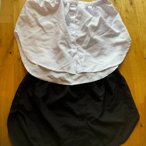 Svart och vit kjol - Säljer två kjolar, en svart och en vit. Båda har en elastisk midja och knappar framtill. Perfekta för vardagsbruk eller att matcha med olika under toppar. De är nya och redo för en ny ägare!