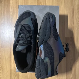 Puma x Skepta Forever sneakers - Säljer ett par Puma x Skepta Forever sneakers i storlek 42.5. Skorna är svarta med en cool, reflekterande yta som skiftar i olika färger beroende på ljuset. De har snörning och en bekväm passform, perfekt för både vardag och fest. Skorna är i nyskick och kommer i originalförpackning.