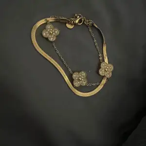 Säljer ett elegant guldarmband med tre blommor dekorerade med pärlor. Armbandet har en fin kedja och en ormlänk som ger en lyxig känsla. Perfekt för festliga tillfällen eller som en fin present.