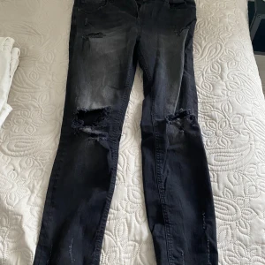 Svarta slitna jeans - Säljer ett par svarta jeans med slitningar på knäna och vid bensluten. Perfekta för en avslappnad och trendig stil. Passar bra till både vardags och fest!