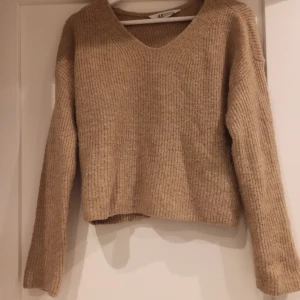 Brun stickad tröja - En fin, mjuk, stickad tröja med en liten V-ringning från H&M.  Storlek 146/152. Passar XS som en croppad tröja med längre ärmar.  Använd ett par gånger, därav fint skick. Smått nopprig, men det går lätt att klippa bort med vanlig sax.  5℅ ull