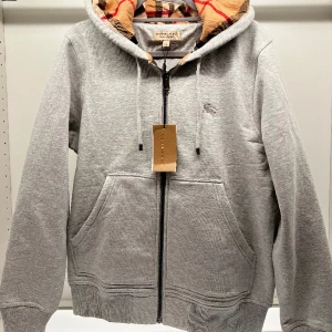 Burberry Hoodie  - Burberry zip hoodie i storlek M men Fits M-L. I fint skick, helt felfri och oanvänd. Grå och mönster invändigt. Pris går att diskuteras vid snabb affär.  (Kan mötas i Stockholm) 