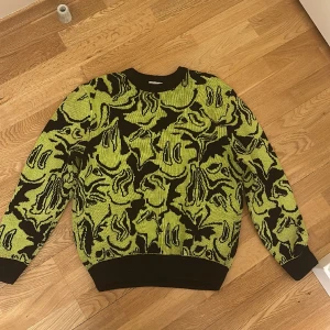 Tjock tröja  - Tröjan är grön och lite svart med smileys på, den ska vara lite oversized så den är stor i storlek. Tröjan är skön att ha på sig och är varm och tjock. 