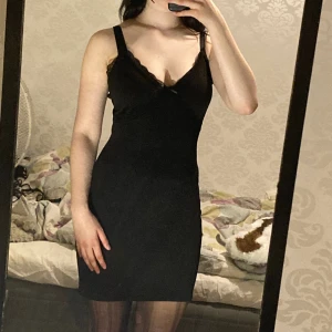 Svart Klänning H&M - Svart klänning från hm med spets och en rosett. Använd 2 gånger kanske men den är aningen för stor för mig och säljer därför. Jag har försökt sy in den i sidorna men har sprettat upp detta men det skadade inte klänningen. 