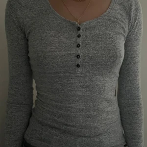Grå långärmad tröja från Hollister - Grå långärmad tröja med bruna knappar och rund krage från Hollister i storlek S.  Tröjan är väldigt skön och lurvig!