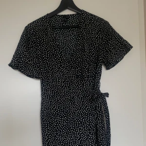 Svart omlottklänning - Söt svart omlottklänning med vita prickar från Veromoda. Klänningen slutar lite över knäna och är prefekt till sommaren. Klänningen är i fint skick!
