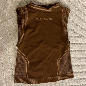 Brun topp - Brun topp från iets frans.. som formar kroppen jättefint, den är inte croptop men är inte heller full längd. Sidorna är typ i mesh så den är jätteluftig och bekväm. 