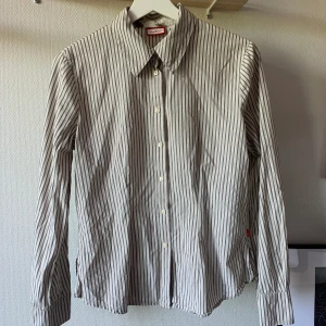 Randig skjorta - Så fin beige och brunrandig skjorta! Den är aningen figursydd och är verkligen perfekt! Coola knappar som är kvadrat formade, har använts väl men är i toppenskick!