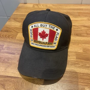 Dsquared2 Keps  - D2 keps ”Fuck All But The Flag”   Skick 8/10 ytterst solblekt använde den 2023 halva sommarn. Köpt för 1700 på nk kvitto o tags finns. 