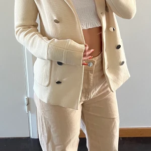 Vacker Gant kofta - En stilig och välvårdad kofta som följer kroppsformen galant! Den är sandvit och har silvriga knappar, det finns två extra knappar till. Modellen är äldre och exklusiv🤩 materialet är 100% ull, ett riktigt kap!