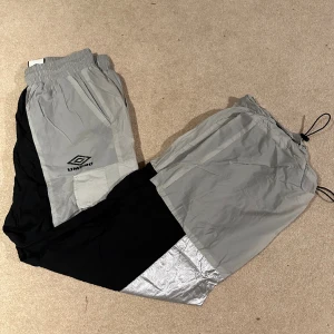 Träningsbyxor - Ett par träningsbyxor i prasselmaterial från UMBRO. Reflex och svarta detaljer. Använda 1 gång.