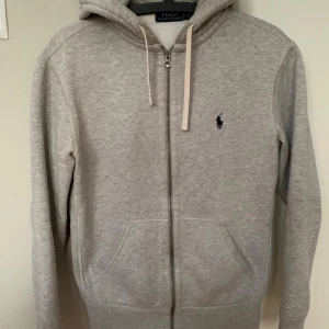 Ralph Lauren huvtröja, stl S - Ralph Lauren Polo Sport luvtröja grå. Köpt på Plick för 600 kr, blev för liten. Är stl S herr, vilket motsvarar stl 164 (modellen på bilderna 174 cm lång). Skickar eller hämtas i Västerås alt Sala. Märkligt möster bild 3, ser ej ut så på riktigt.