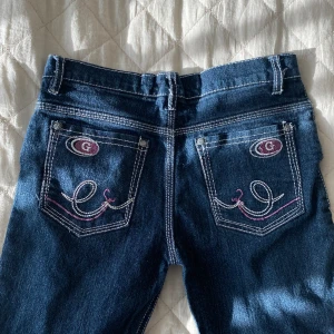 Vintage jeans med vita sömmar - Jättesöta raka, lågmidjade mörkblå jeans med vita sömmar och snyggt rosa mönster på fickorna. Skulle säga storlek xs Längd 93  Innerbenslängd 68  Midjemått 36