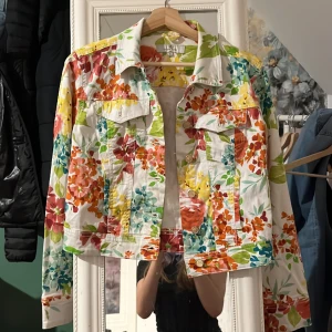 Blommig jeansjacka  - Snygg croppad jeansjacka med färgglatt blommönster. Från Flash Jeans i S. Praktiskt taget oanvänd