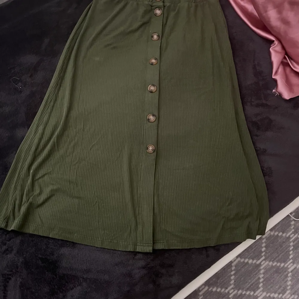 Grön kjol med knappar, lite över knäna, tajt i övre delen men lite större i nedre. Används bara några gången . Kjolar.