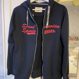 Hoodie med dragkedja - Mörkblå hoodie med rosa text och dragkedja. I storlek XL/42