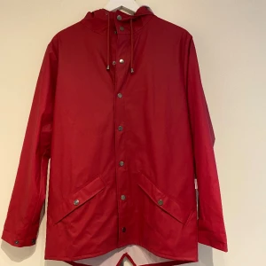 Regnjacka från Rains i stl XXS/XS - Säljer denna röda regnjacka från Rains i stl XXS/XS. Upplevs som stor i storleken. Inköpt 2019 men använd ett fåtal gånger. Jackan stängs med bara knappar.