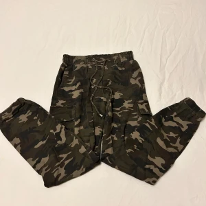 Kamouflage cargo byxor  - Ganska bra skick förutom att en av knapparna har gått av som man kan se i andra bilden, väldigt stretchig Storlek 32 100kr + frakt