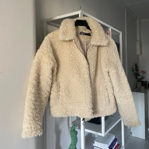 Kort teddyjacka strl S - Vit/beige teddyjacka från Zara i storlek S. Använd men i mycket fint skick, enda är att den lilla grejen man hänger jackan på en krok med, har gått av. 